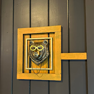 Brass bear bust in yellow spectacles, mounted in a mustard wood frame